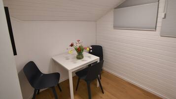 Een gezellig eethoekje met een witte tafel en twee zwarte stoelen, een vaas met bloemen, en een raam met zonwering.