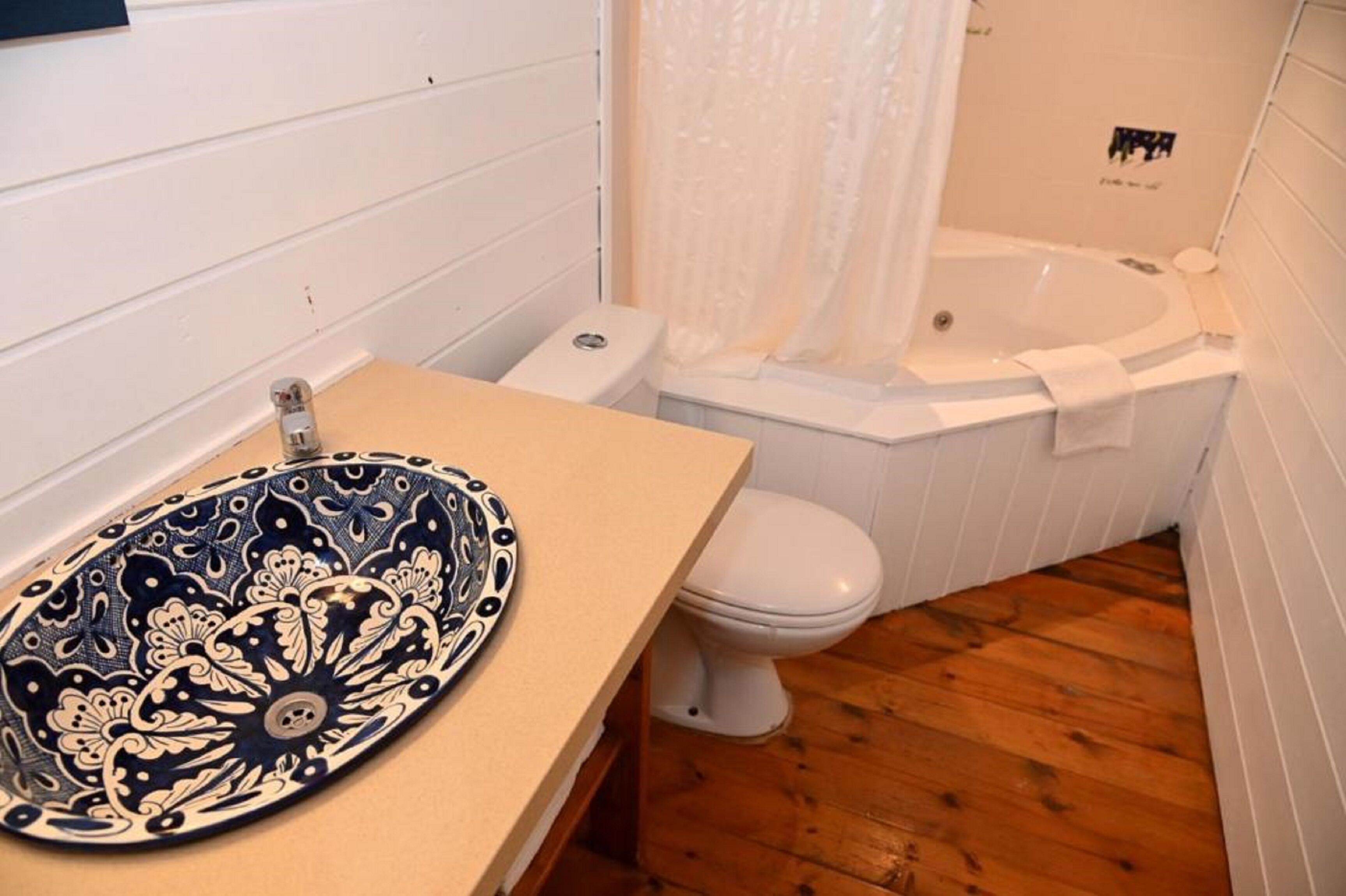 A bathroom with a wooden floor, a white toilet, a white bathtub, and a sink with a decorative bowl.