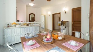 Un'area pranzo con un tavolo in legno apparecchiato per quattro persone, circondato da sedie bianche. Si nota una ventola a soffitto sopra il tavolo.