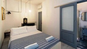 Una camera da letto con un letto, un comodino, una sveglia e una porta che dà su un bagno.