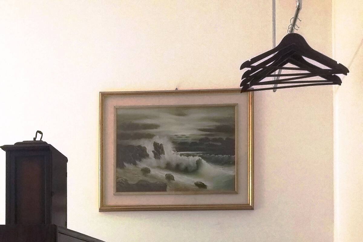 Ein Zimmer mit einem Holzkasten, einem gerahmten Gemälde, einer Bank und einem Kleiderständer.