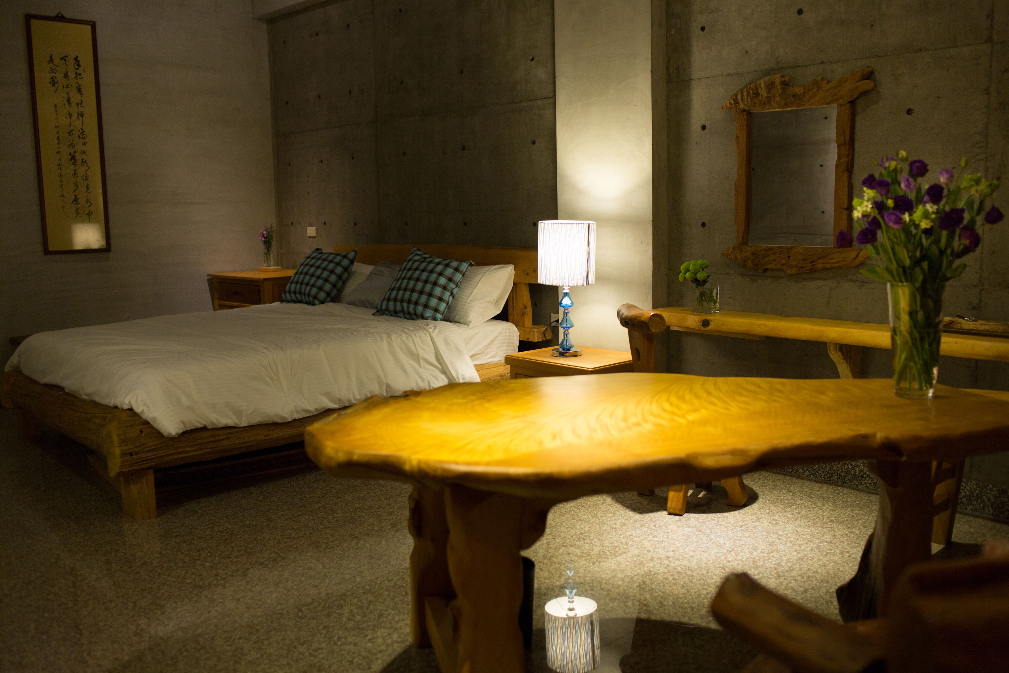 A hotel room with a bed, bedside table, lamp, and a small table with a vase of flowers.
