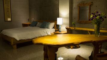 A hotel room with a bed, bedside table, lamp, and a small table with a vase of flowers.