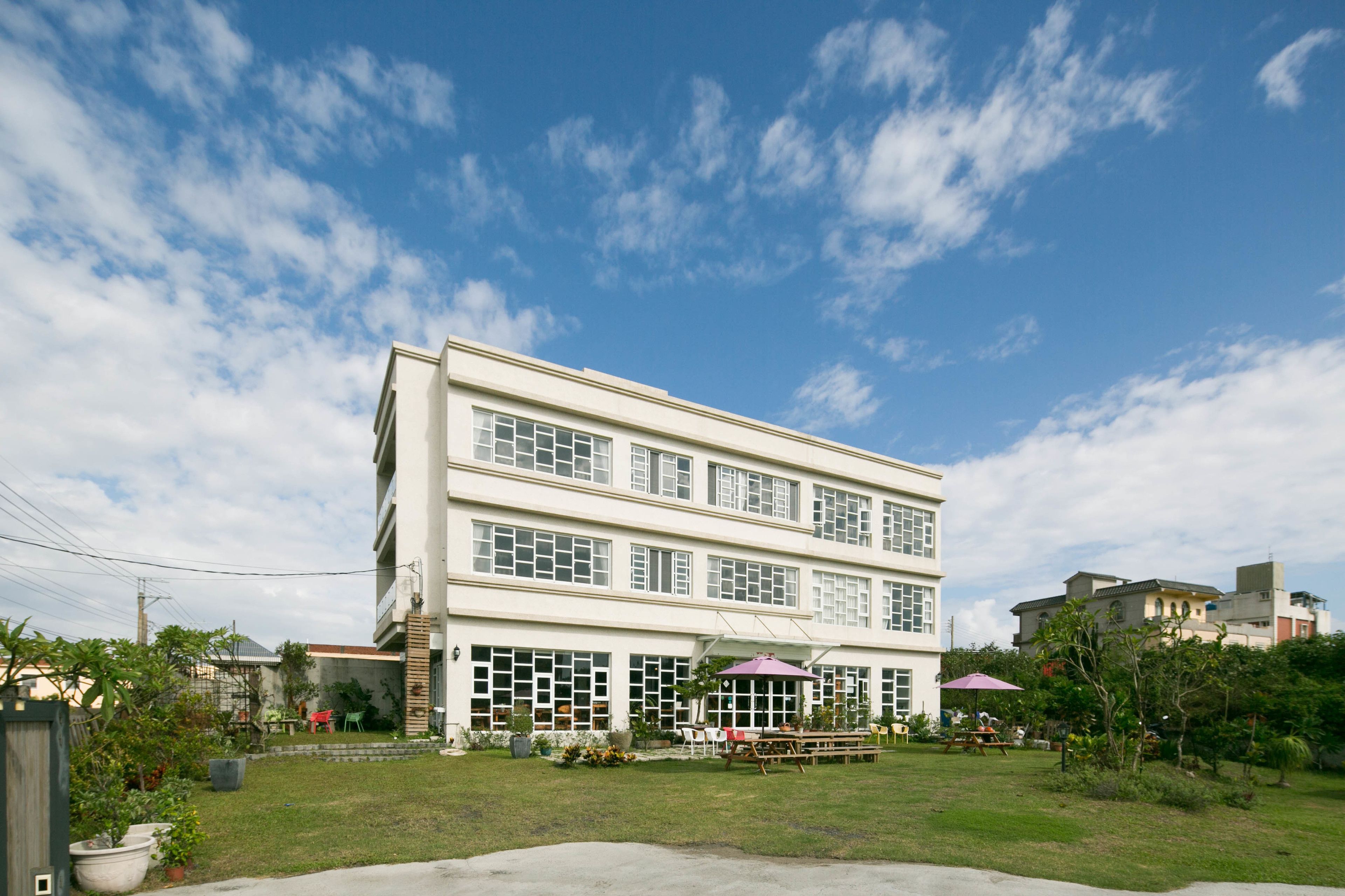 A two-story building with a flat roof, large windows, and a covered outdoor seating area with umbrellas.
