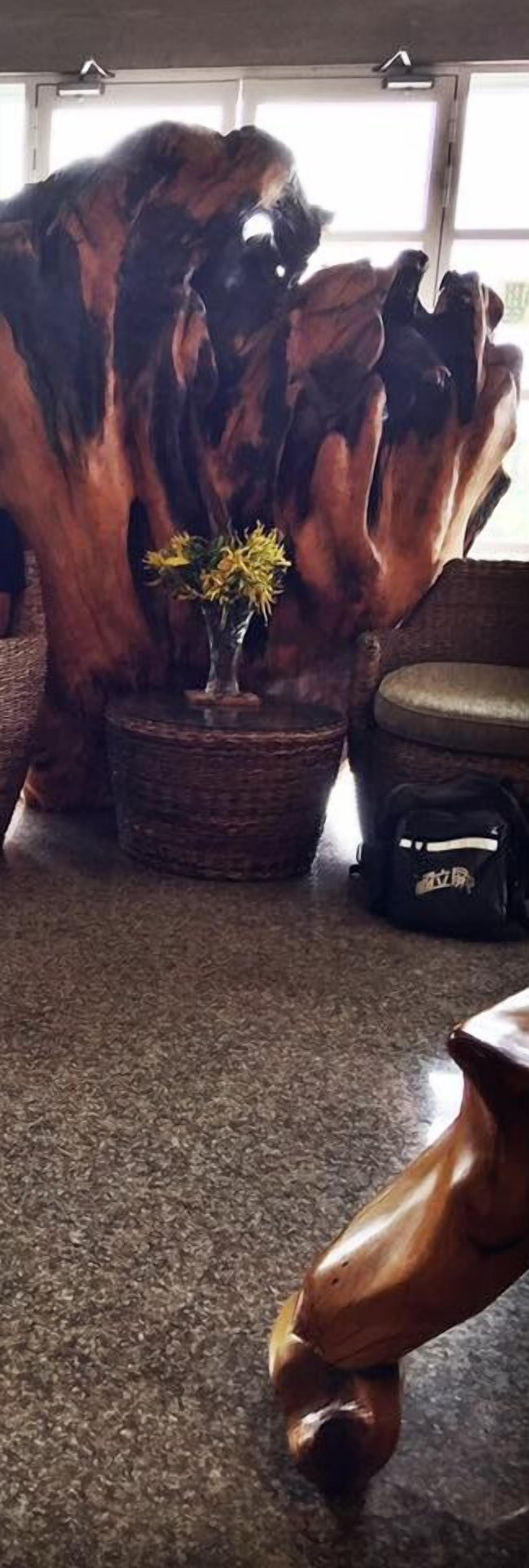 Ein Zimmer mit einer großen Holzskulptur, einem kleinen Tisch mit Blumenvase und einer schwarzen Tasche auf dem Boden.