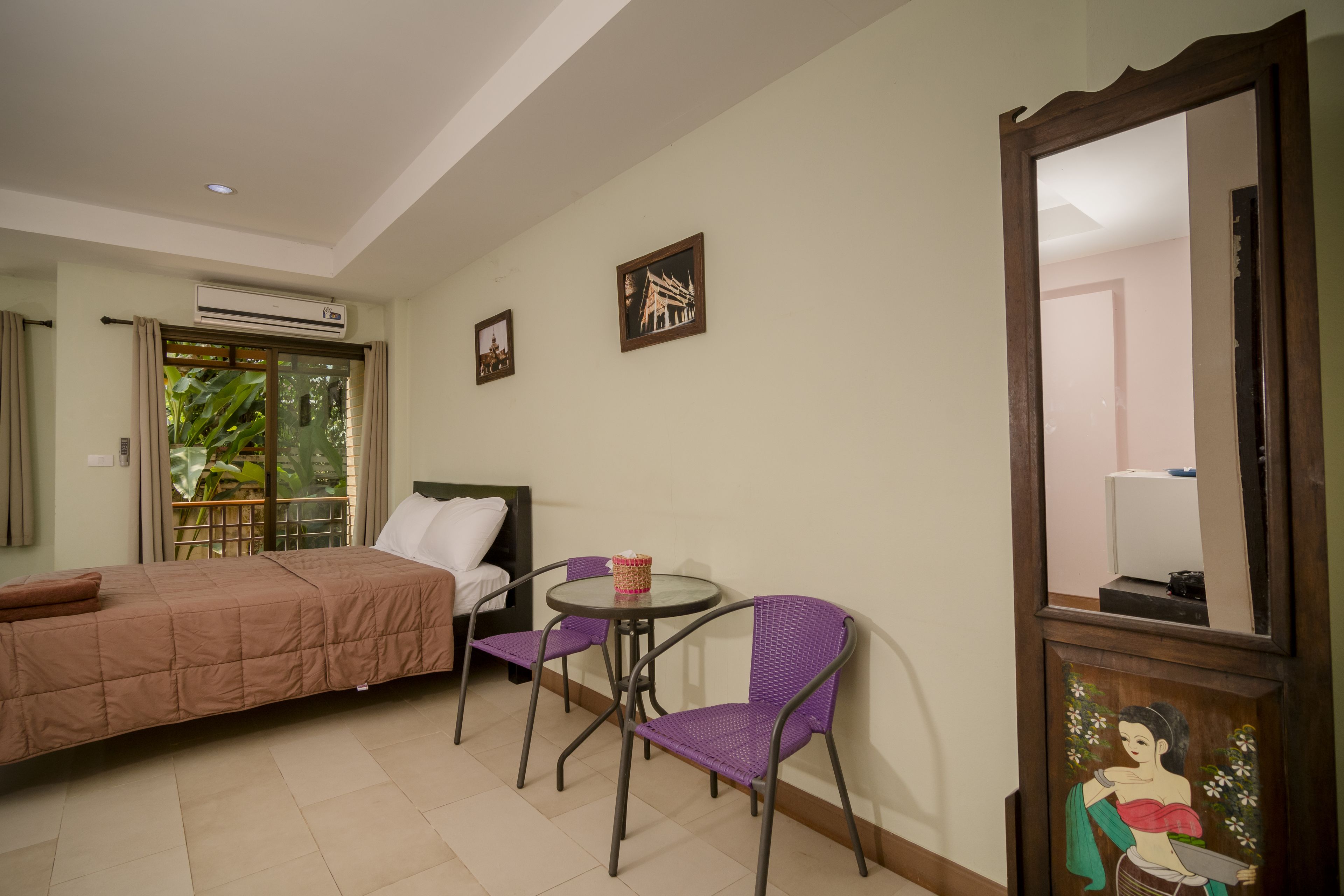 A hotel room with a bed, two chairs, a small table, and a large mirror.