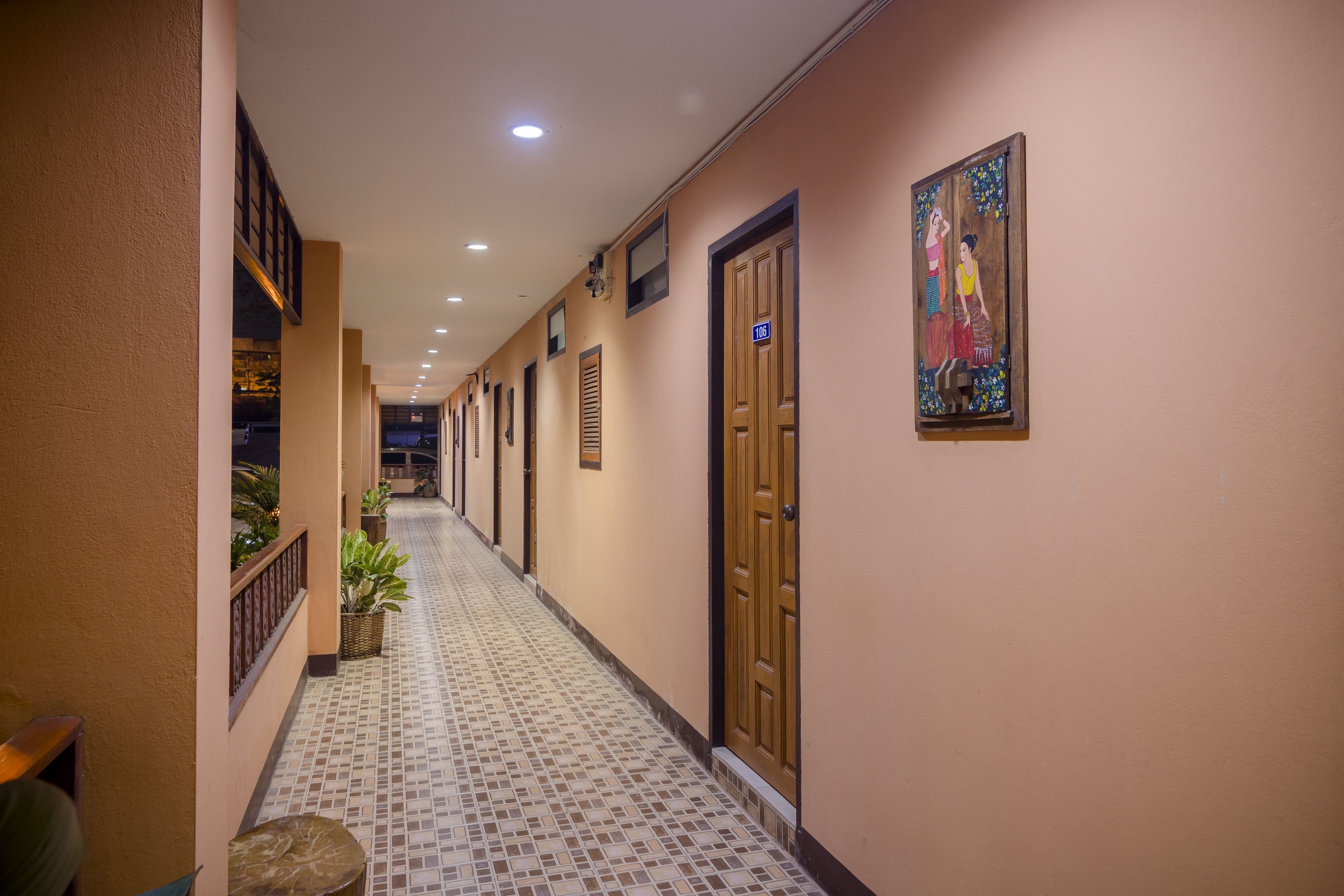 A hotel corridor with tiled flooring, wooden doors, and a framed artwork on the wall.