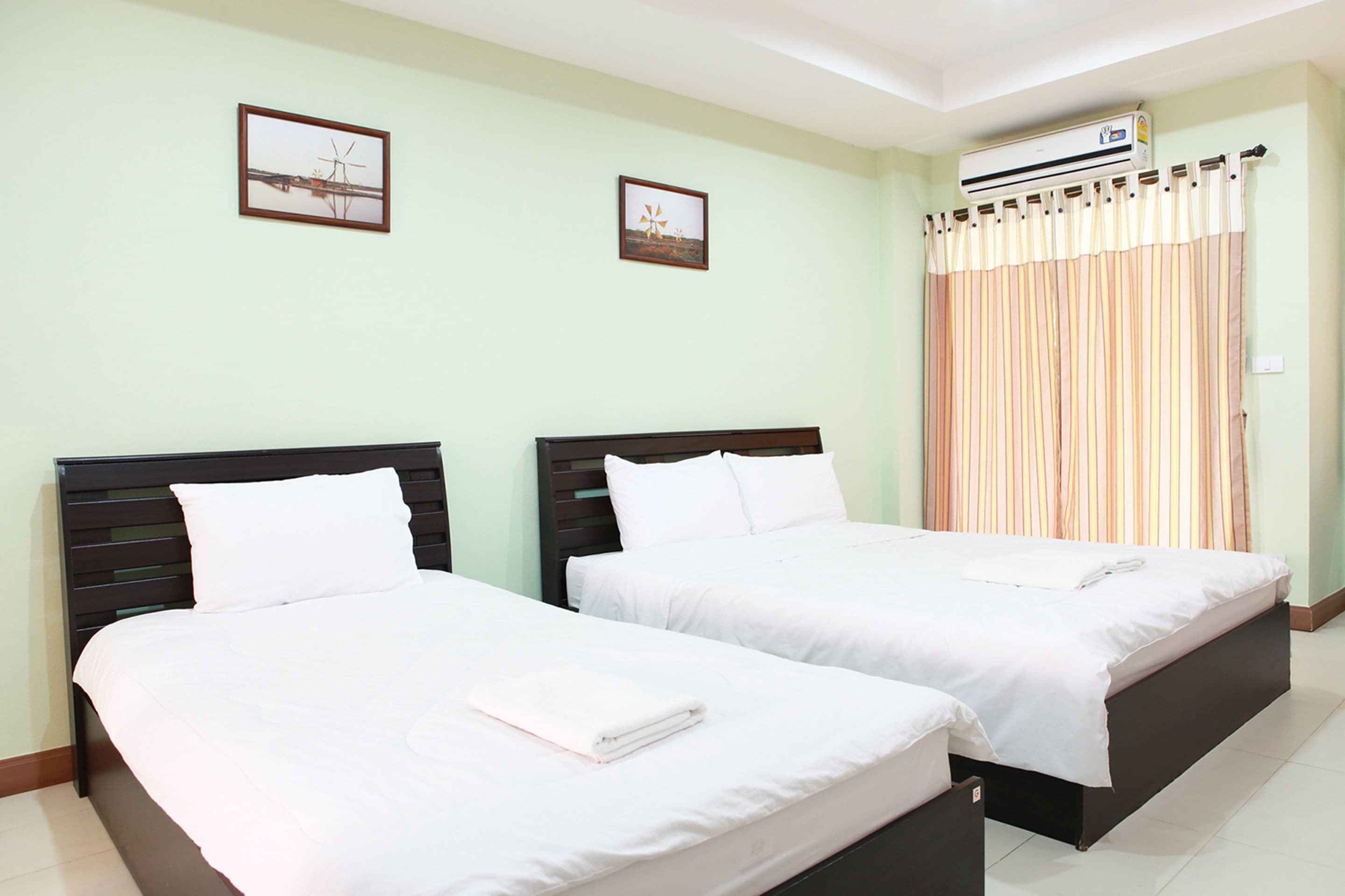 A hotel room with two beds, a window with curtains, and an air conditioning unit on the wall.