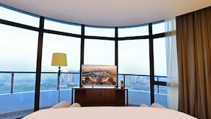 A hotel room with a large bed, a television on a wooden stand, and a view of a cityscape through large windows. - Grand Skylight Int'l Hotel Huizhou (Huizhou)