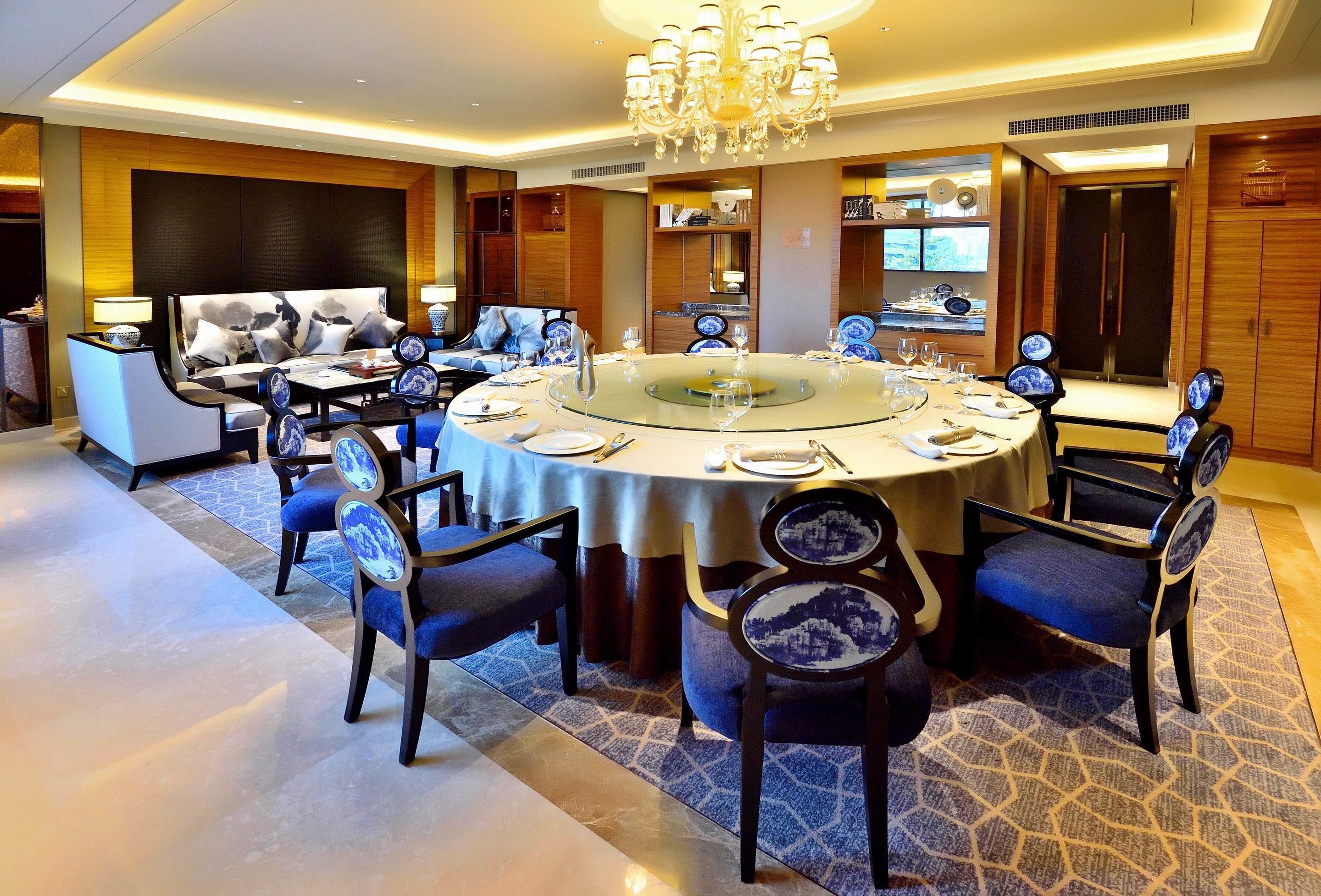 A modern dining area with a round table, blue upholstered chairs, and a chandelier.
