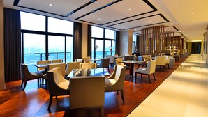 A modern hotel lobby with a long, polished wooden floor, large windows offering a city view, and a variety of seating arrangements including tables and chairs. - Grand Skylight Int'l Hotel Huizhou (Huizhou)