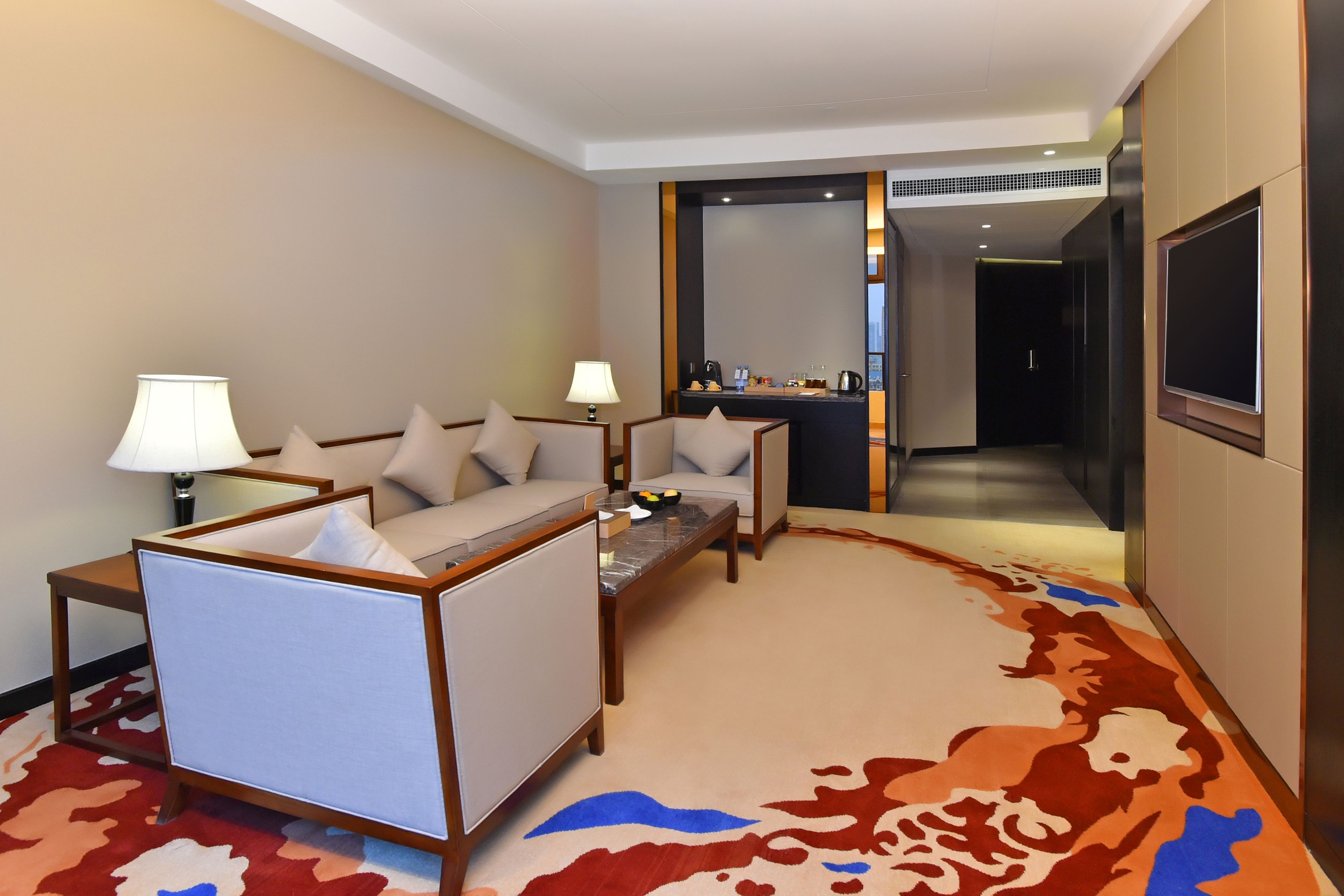 A hotel room with a sofa, two armchairs, a small table, and a desk with a mirror.