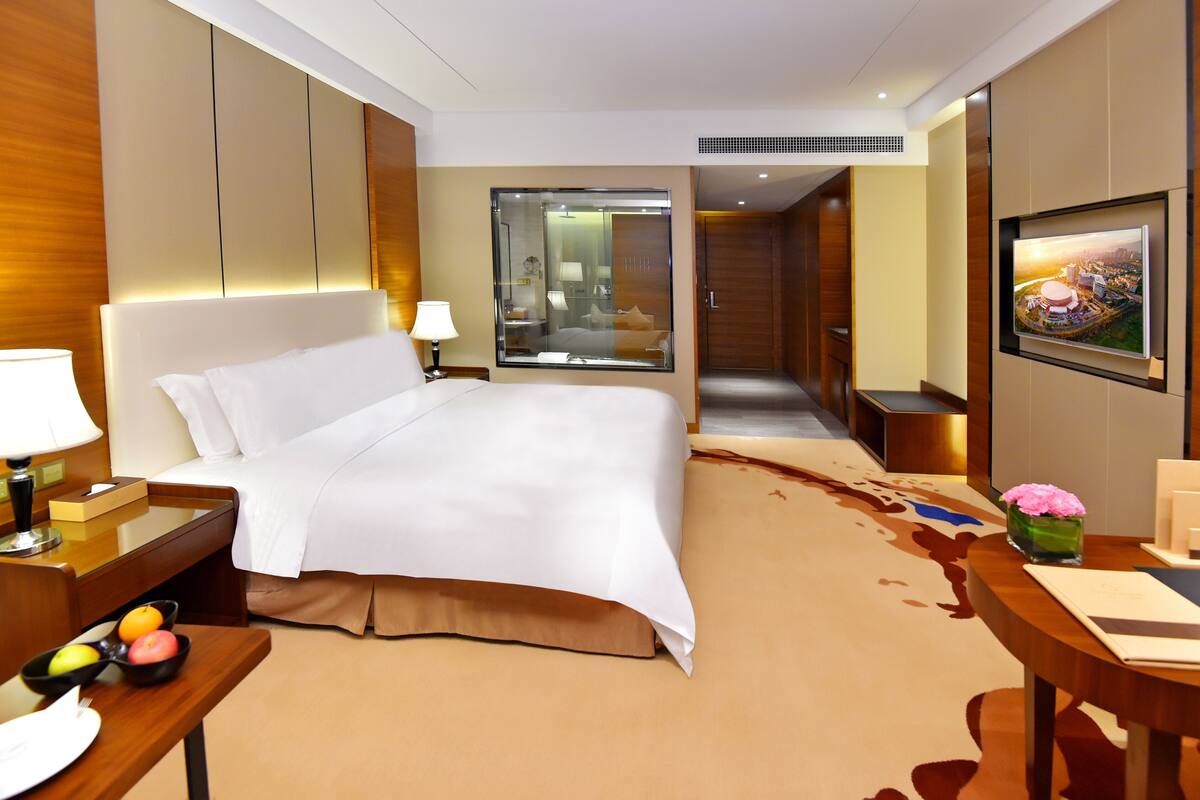 A hotel room with a large bed, bedside table, lamp, and a TV mounted on the wall.