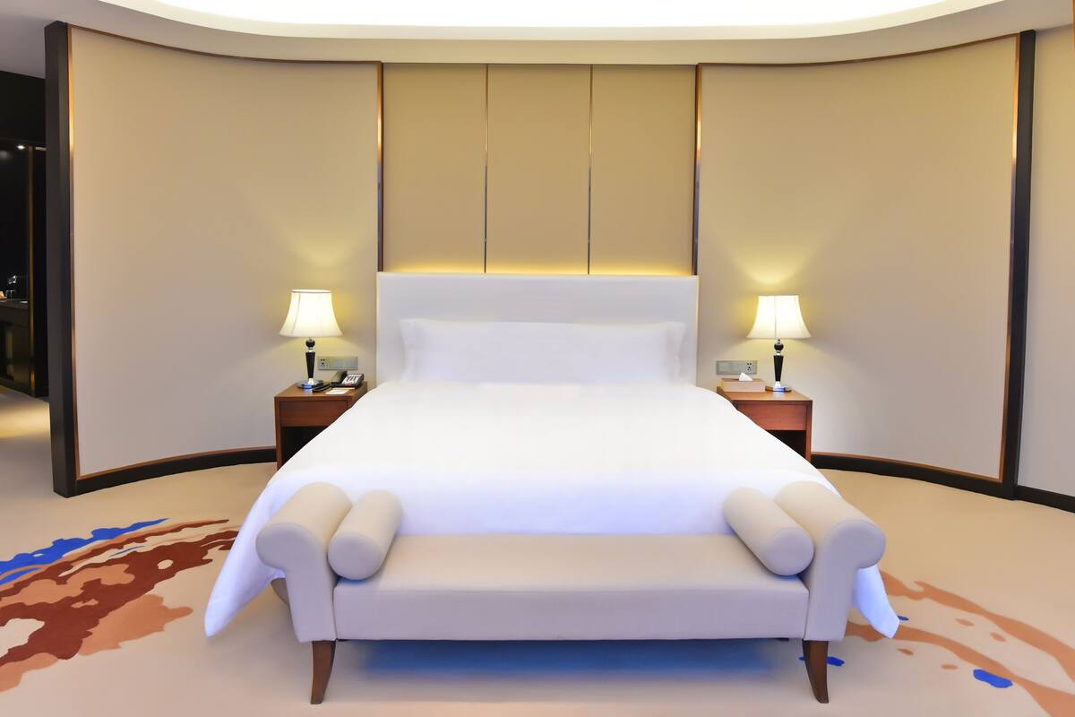 A modern hotel room with a large bed, two bedside tables with lamps, and a unique carpet design.