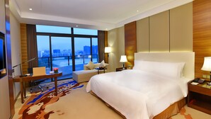 A hotel room with a large bed, a desk with a chair, a sofa, and a view of the cityscape through large windows. - Grand Skylight Int'l Hotel Huizhou (Huizhou)