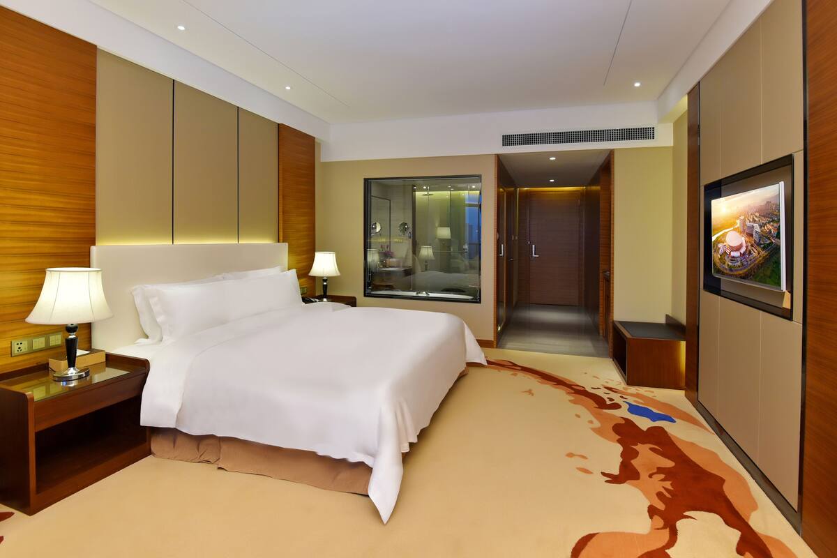 A hotel room with a large bed, bedside lamps, a glass-enclosed shower, and a framed picture on the wall.