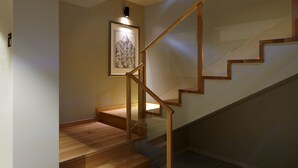 Un escalier en bois avec une rampe en verre, une œuvre d’art encadrée accrochée au mur et un luminaire placé au-dessus.