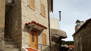 Un bâtiment en pierre avec un toit en tuiles, des volets en bois et une rue pavée.