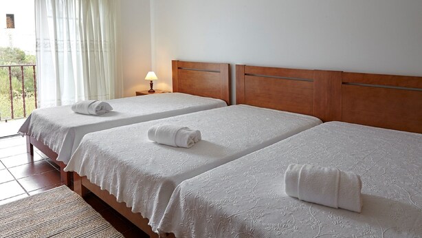 A hotel room with two single beds, each with a white bedspread and a rolled towel on the bed. There is a nightstand with a lamp between the beds. - Abrigo da Montanha Alojamento Familiar (Seia)