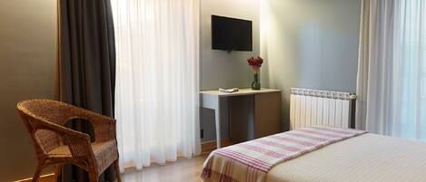 A hotel room with a bed, a desk, a chair, a TV, and a window with curtains.