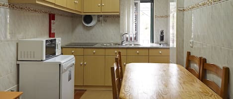Una cocina compacta con armarios de madera, microondas, pileta y una mesa de comedor.