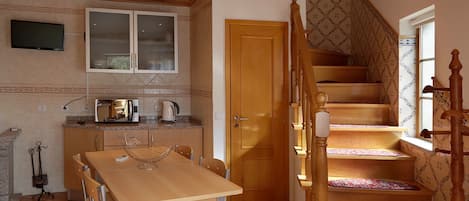A compact kitchen with a dining table, chairs, a microwave, and a kettle. A wooden staircase with patterned carpet leads to a door.