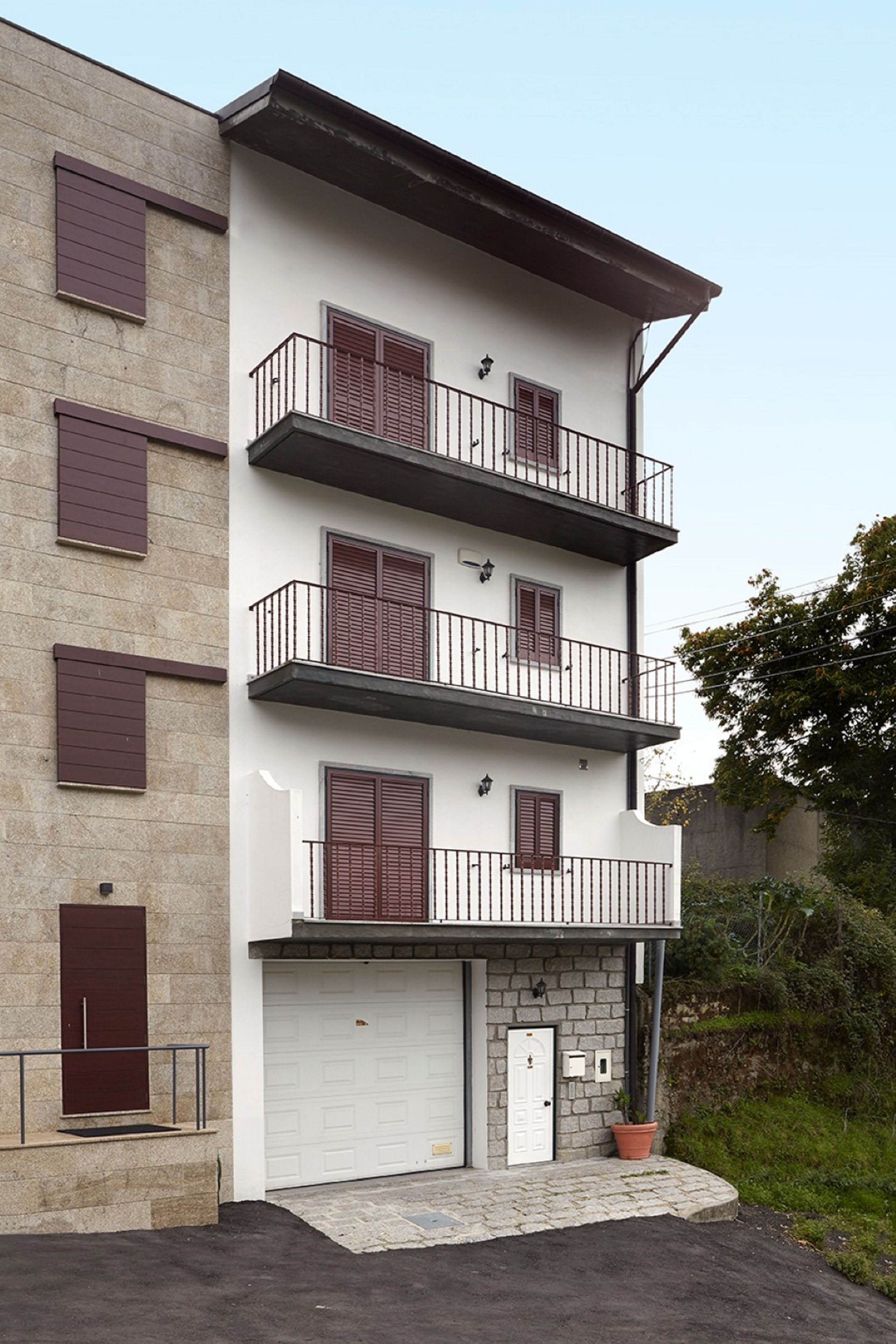 Ein mehrstöckiges Wohngebäude mit weißer Fassade, roten Fensterläden und Balkonen.