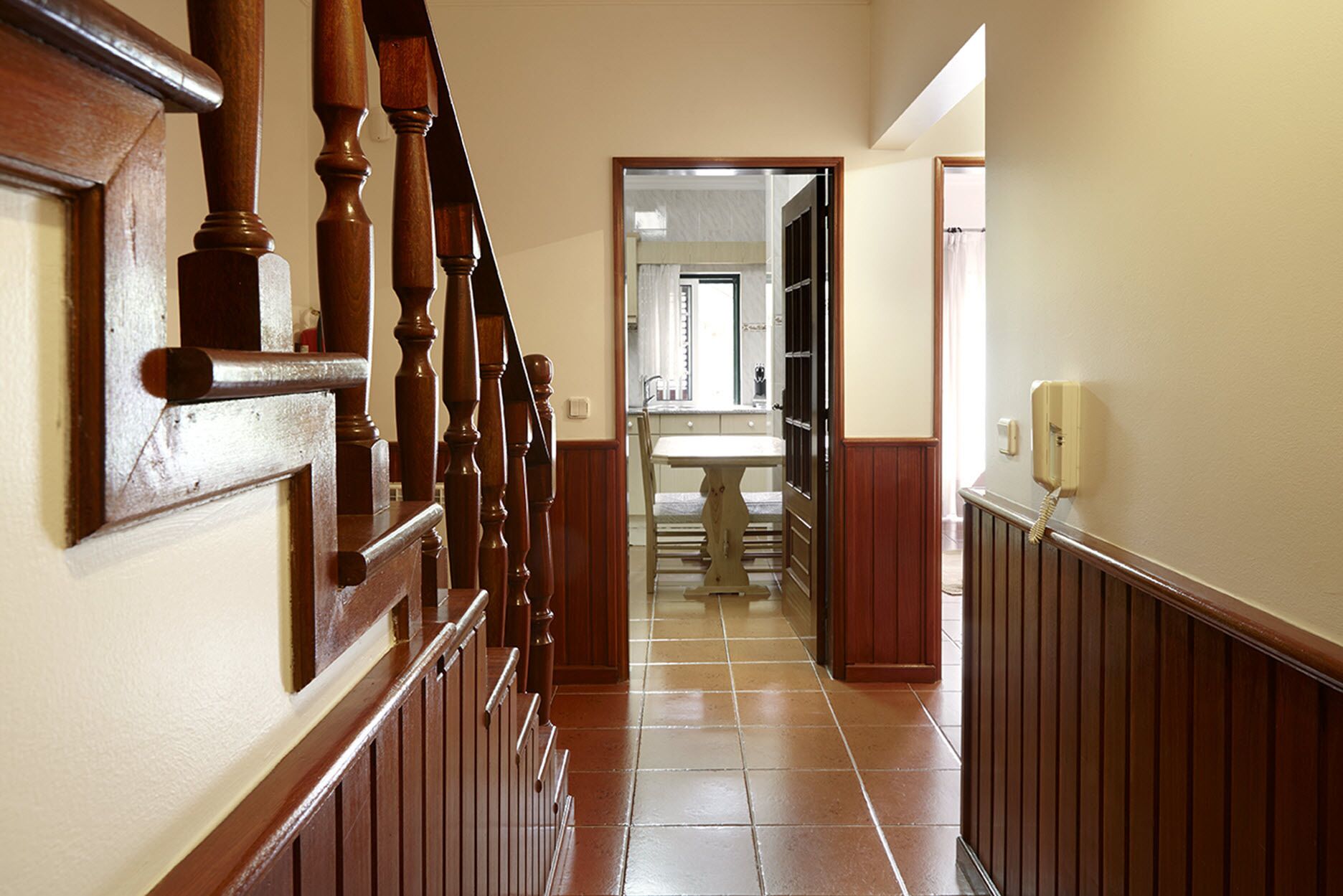 A hallway with a wooden staircase, a tiled floor, and a bathroom visible in the background.