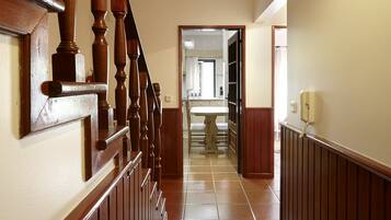 A hallway with a wooden staircase, a tiled floor, and a bathroom visible in the background.