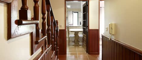 A hallway with a wooden staircase, a tiled floor, and a bathroom visible in the background.