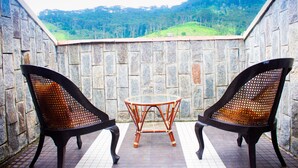 Un balcon avec deux fauteuils en osier et une petite table, donnant sur un paysage vallonné.