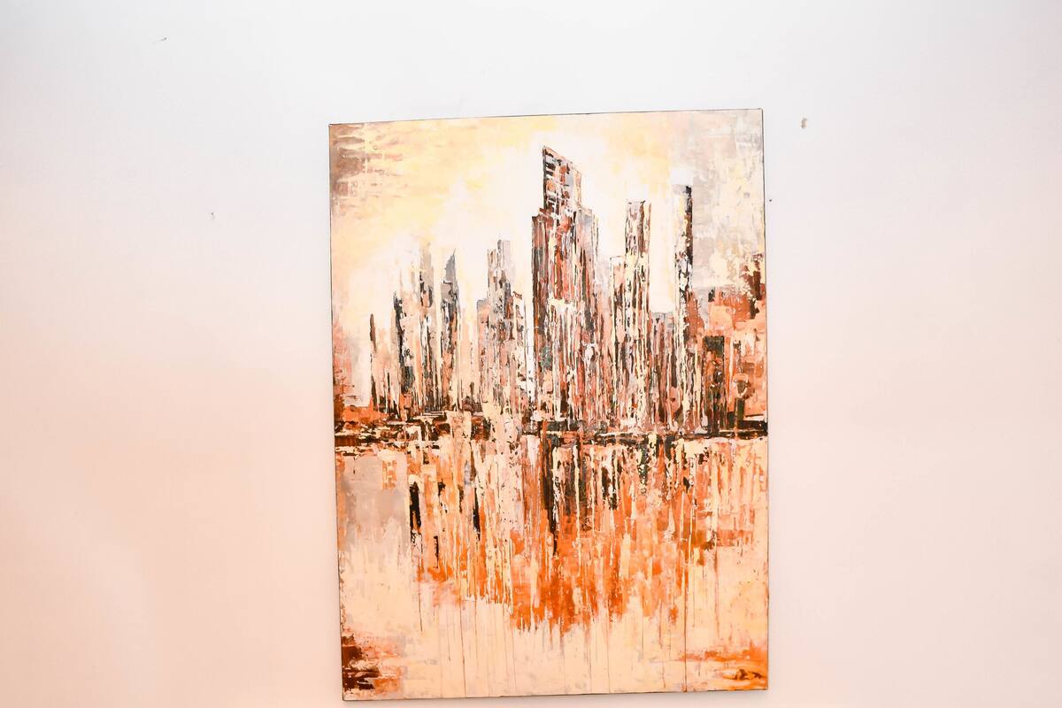 Un lit avec une literie blanche et deux oreillers rouges, un mur blanc et un tableau représentant un paysage urbain.