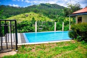 A swimming pool with a view of green hills and a building in the background. - Sri Kandyan Bungalow (Kandy)
