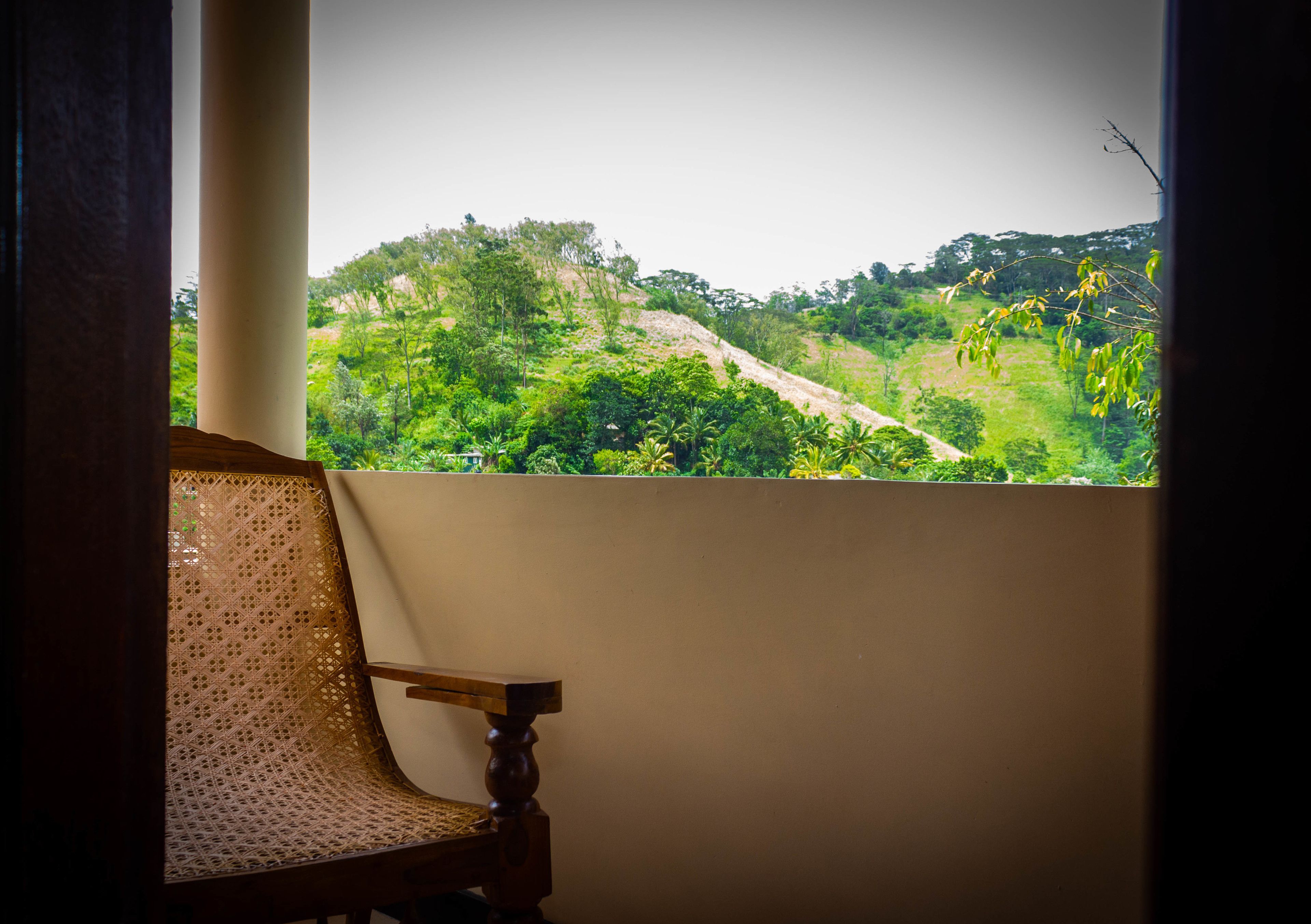 Vista desde una ventana con una silla de madera, sobre un exuberante paisaje con colinas verdes.