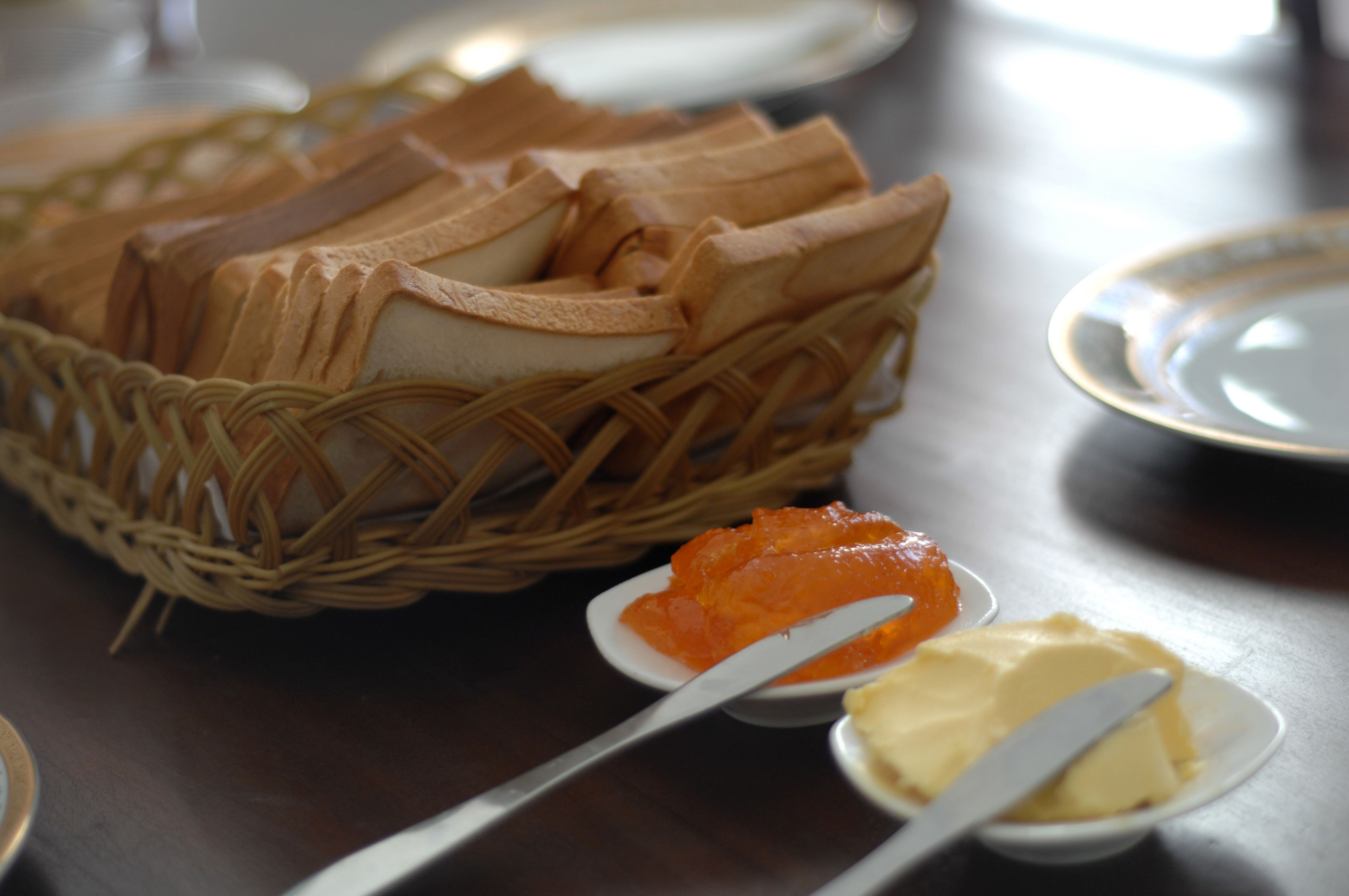 A wicker basket filled with bread rolls, a small bowl of orange spread, and a small bowl of butter on a table.