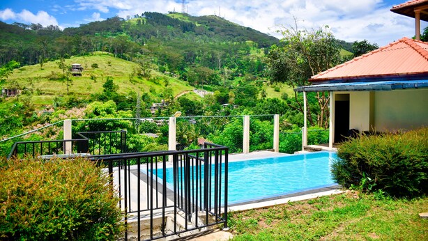 Une piscine bordée d’une rambarde en métal, entourée d’une végétation luxuriante et avec des collines en arrière-plan.