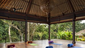 An open-air yoga studio with wooden flooring, yoga mats, and cushions arranged for practice. - Adiwana Resort Jembawan (Ubud)