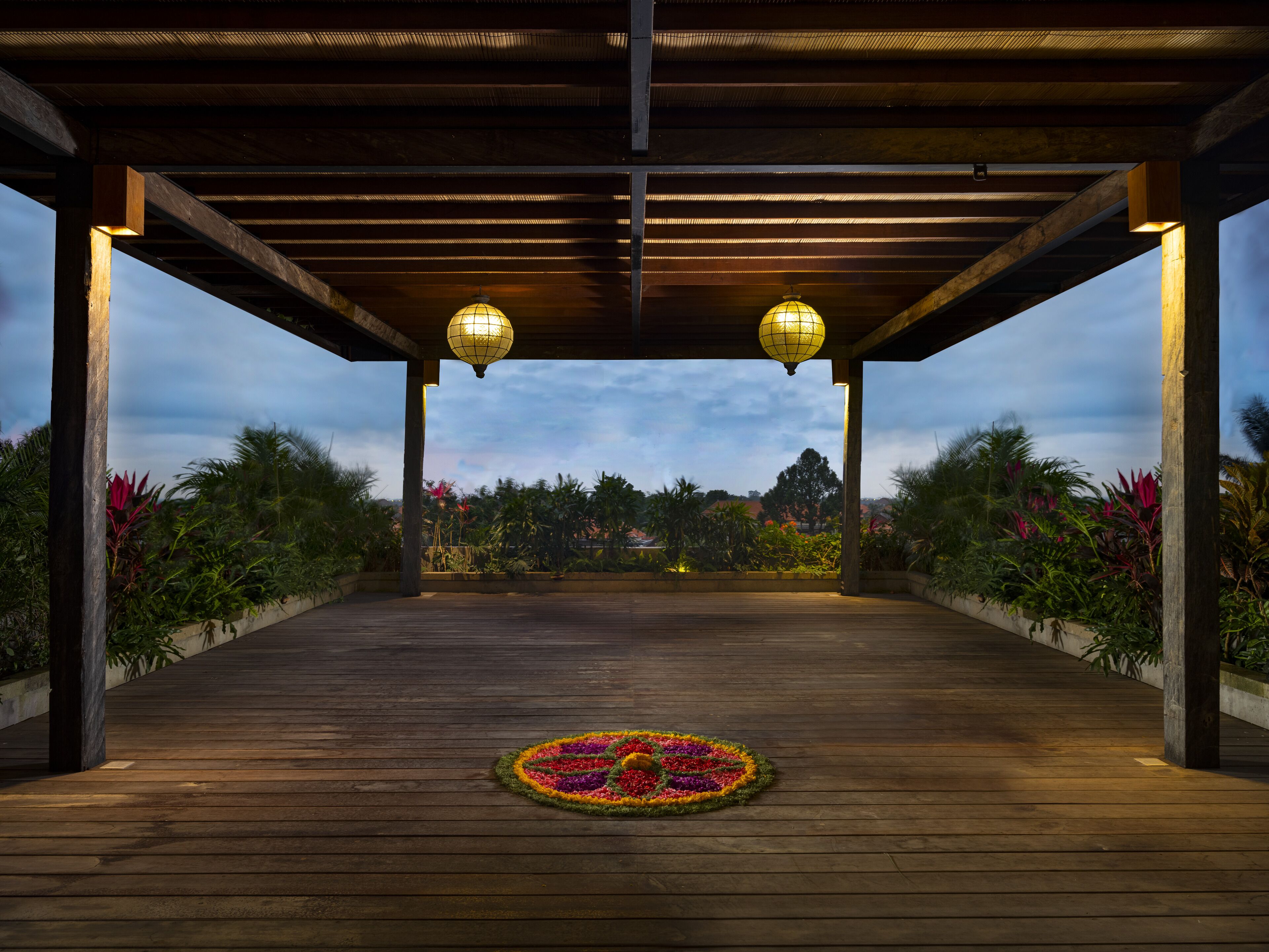 Um deck de madeira aberto com um padrão floral decorativo no centro, sob uma pérgola de madeira com duas lanternas penduradas.