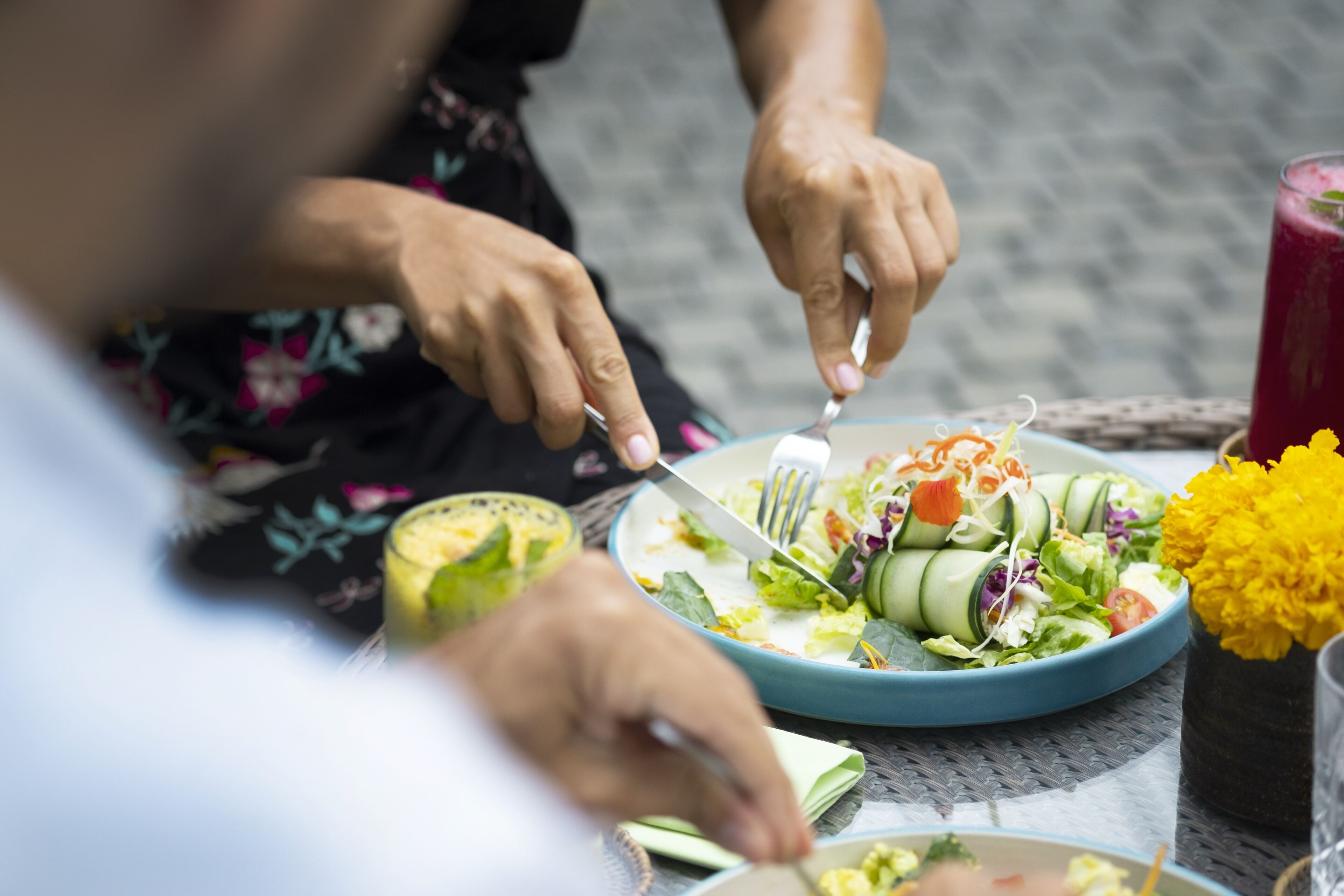Una persona comiendo una ensalada con un tenedor y un cuchillo sobre una mesa.