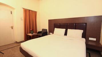 Una habitación de hotel con una cama grande, una mesita con un jarrón, una silla y una puerta.