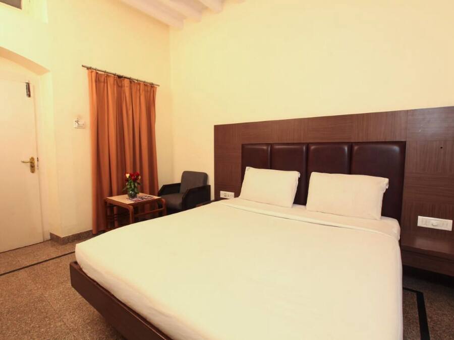 Una habitación de hotel con una cama grande, una mesita con un jarrón, una silla y una puerta.