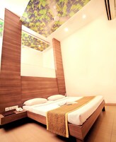 A modern bedroom with a wooden headboard, a bedside table with a phone and book, a bed with a patterned throw, and a ceiling with a leaf design.