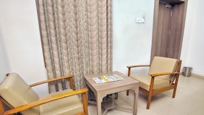 A room with two wooden chairs, a small table, and a patterned curtain. - Taj Mahal Hotel Abids (Hyderabad)