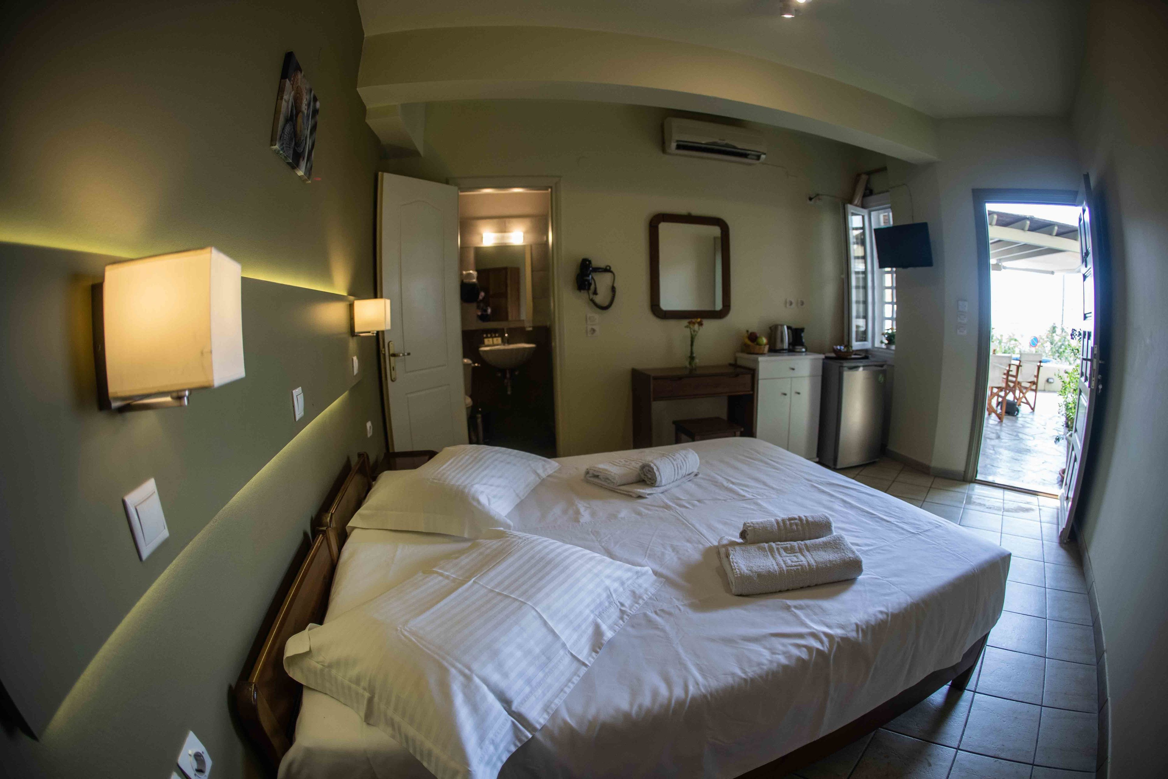 A hotel room with a large bed, a bathroom with a mirror, and a TV on the wall.