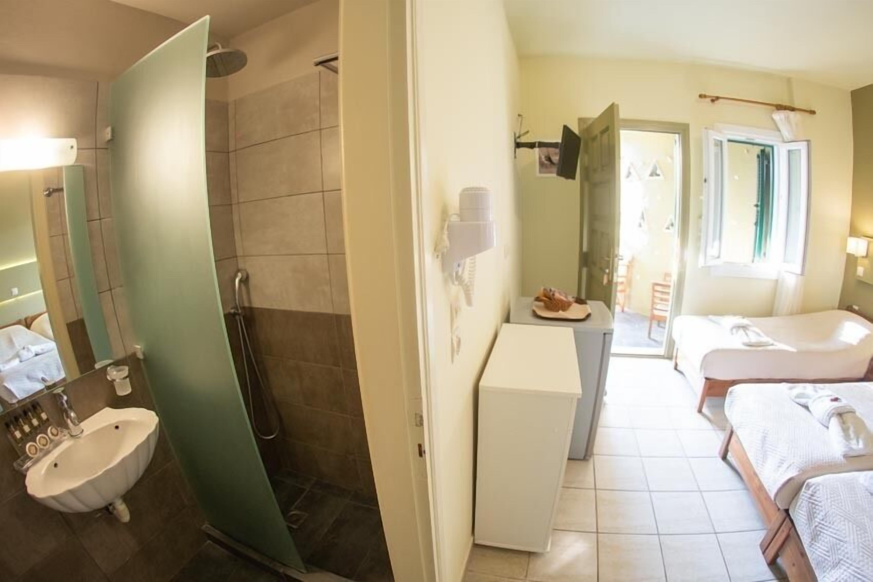 A hotel room with a shower, a sink, a small table with a plate, a bed, and a bedside table.