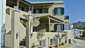 Un bâtiment à deux étages doté d’un balcon, de plantes en pot et d’une enseigne sur laquelle on peut lire « Filoxenia ».