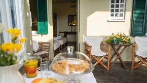 Une table dressée pour le petit-déjeuner, avec une table, des chaises, un pichet de fruits, un verre de jus, un présentoir couvert pour les aliments et une petite table décorée de fleurs.