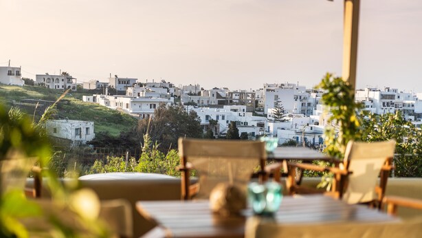 Une terrasse dotée de mobilier en bois et offrant une vue sur des bâtiments blancs en arrière-plan.