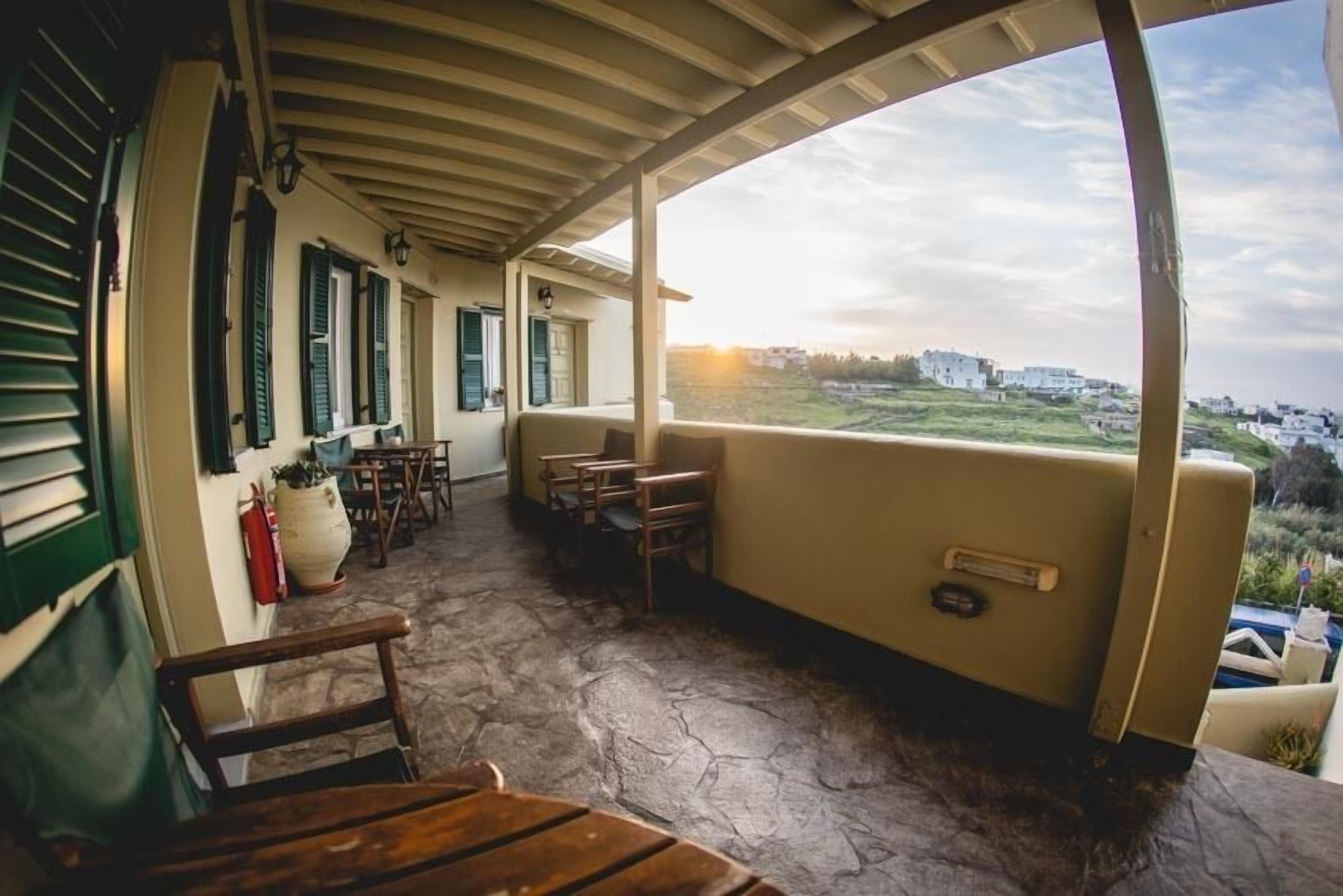 Een overdekt terras met stenen vloer, houten meubels en uitzicht op een kustlandschap.