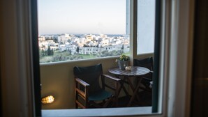 Un balcon donnant sur un paysage urbain, une table, deux chaises et une plante en pot.